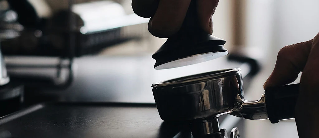 Barista applying pressure with a high-quality espresso tamper for even coffee bed