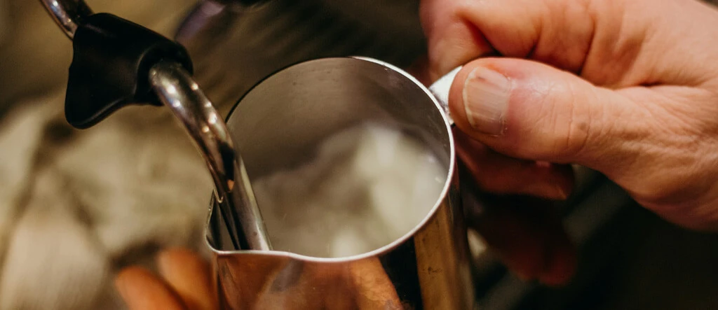Barista pouring froth onto coffee, demonstrating the use of a top milk frother for a perfect brew.