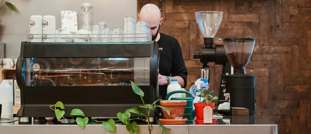 A barista operating an espresso machine with a coffee grinder nearby.