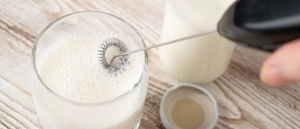 A handheld milk frother being used to whip milk into a creamy froth, showcasing its efficiency and ease of use for home baristas.
