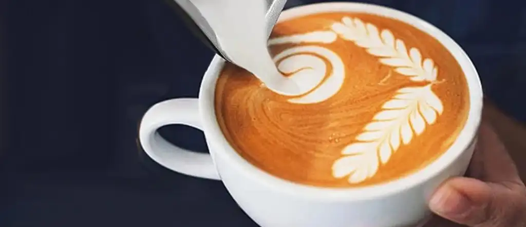 The intricate process of creating latte art with perfectly frothed milk being poured into a cup of espresso, highlighting the artistry in coffee preparation.
