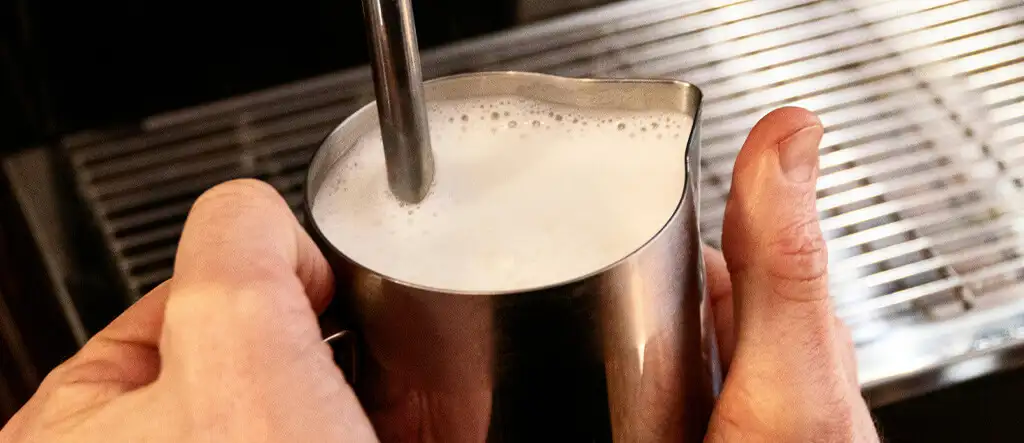 Barista frothing milk in a stainless steel milk jug