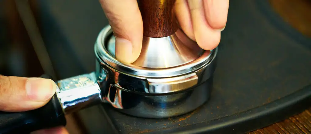 Barista tamping ground coffee in a portafilter to make espresso