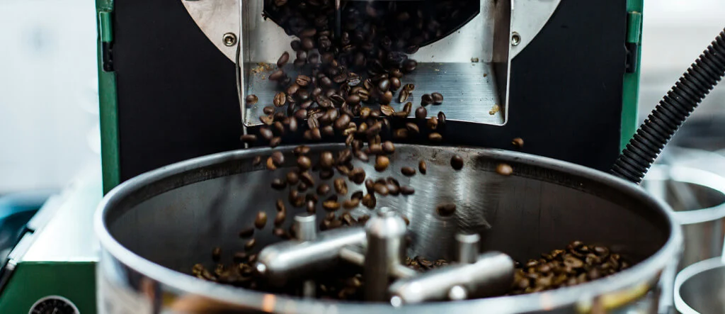 Coffee beans being ground in a large grinder, illustrating the importance of personal taste preferences when choosing coffee beans for espresso.