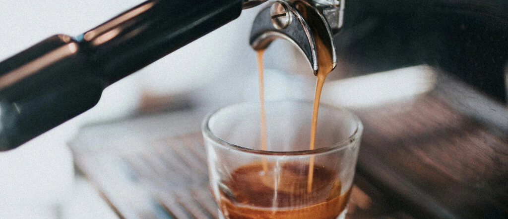 Coffee pouring from an espresso machine into a shot glass