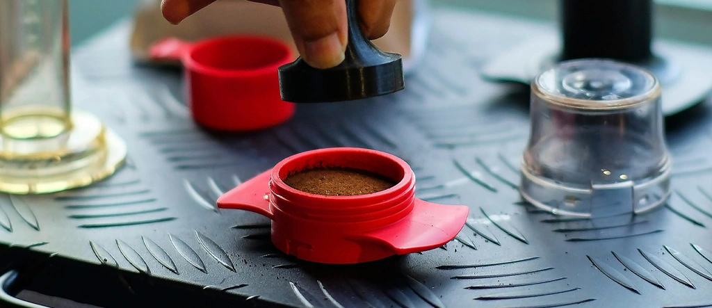 Barista about to press coffee grounds with a tamper