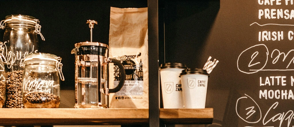 Coffee cups, glass canisters, and a coffee plunger arranged neatly on a shelf.