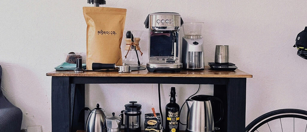 A cozy home coffee bar setup with a coffee maker, mugs, and decor on a wooden shelf.