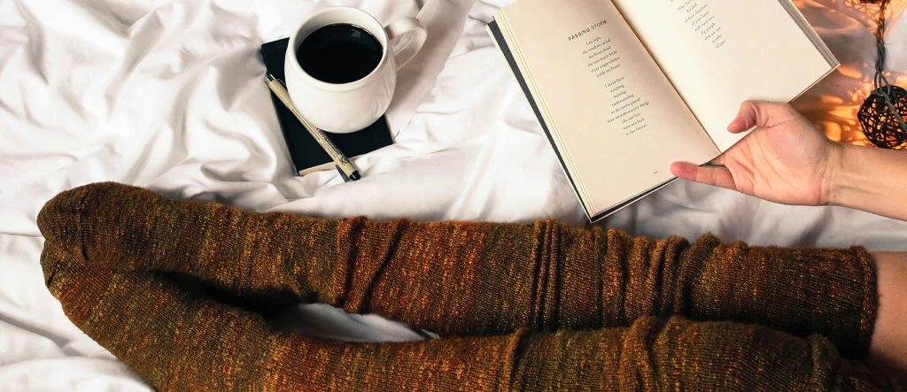 A woman lying on her bed, relaxing with a cup of coffee placed on the bed beside her.