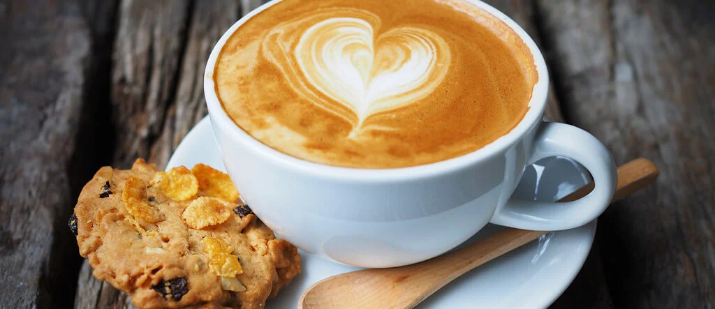 A cup of coffee served with a biscuit on a saucer