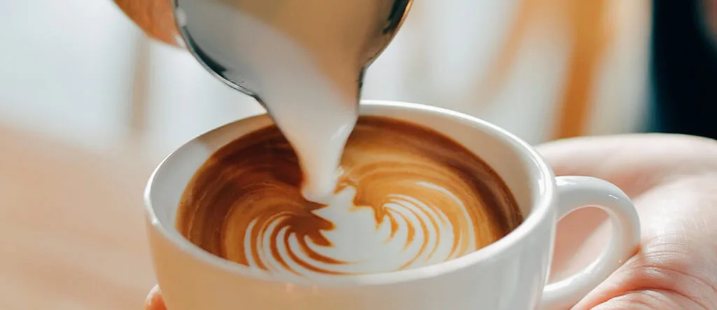 Milk being poured into a freshly brewed cup of espresso