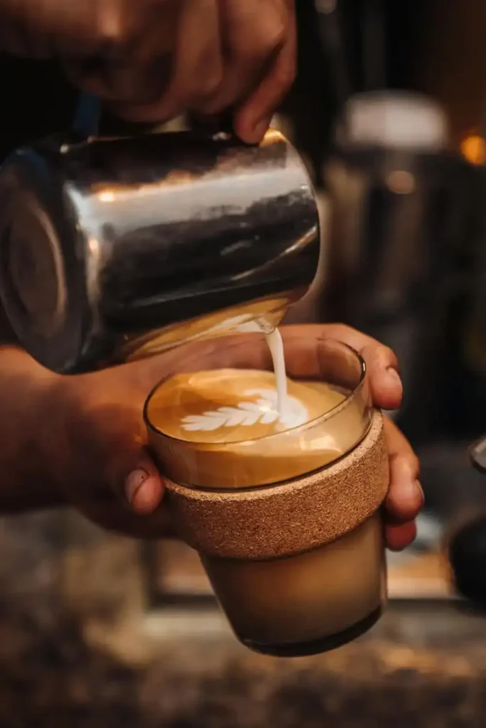 Milk being poured into a latte from a stainless steel milk jug