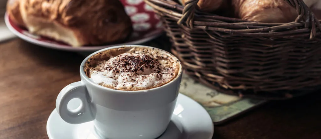 A freshly made cappuccino in a ceramic cup sitting on a wooden bench.