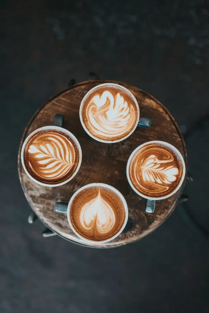 Four different coffee drinks, each in a unique cup, sitting on a table, showcasing a variety of espresso-based beverages.