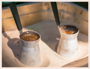 Two Traditional Cups of Turkish Coffee – Strong and Rich Coffee Experience Two traditional cups of Turkish coffee with foam and copper coffee pots in sand
