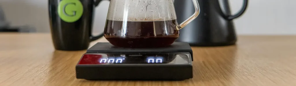 How to Use a Coffee Scale for Better Brews 78 A glass carafe of freshly brewed coffee sitting on a digital coffee scale on a wooden countertop