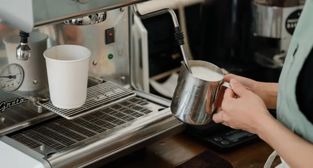 🥛 How to Steam Milk Like a Barista (Beginner-Friendly Guide) 68 Barista showing how to steam milk using a milk pitcher under a steam wand to create microfoam.