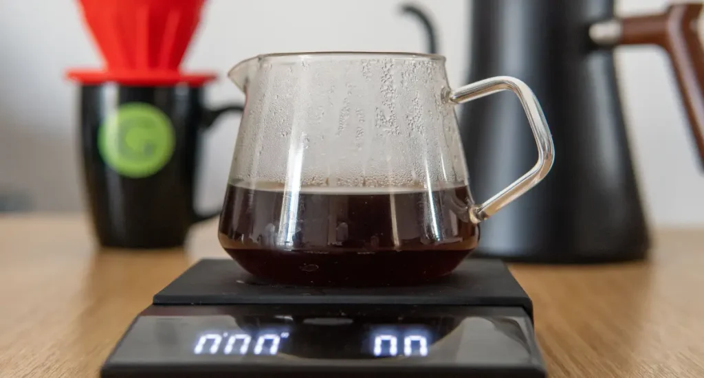 How to Use a Coffee Scale for Better Brews 72 A glass carafe of freshly brewed coffee sitting on a digital coffee scale on a wooden countertop