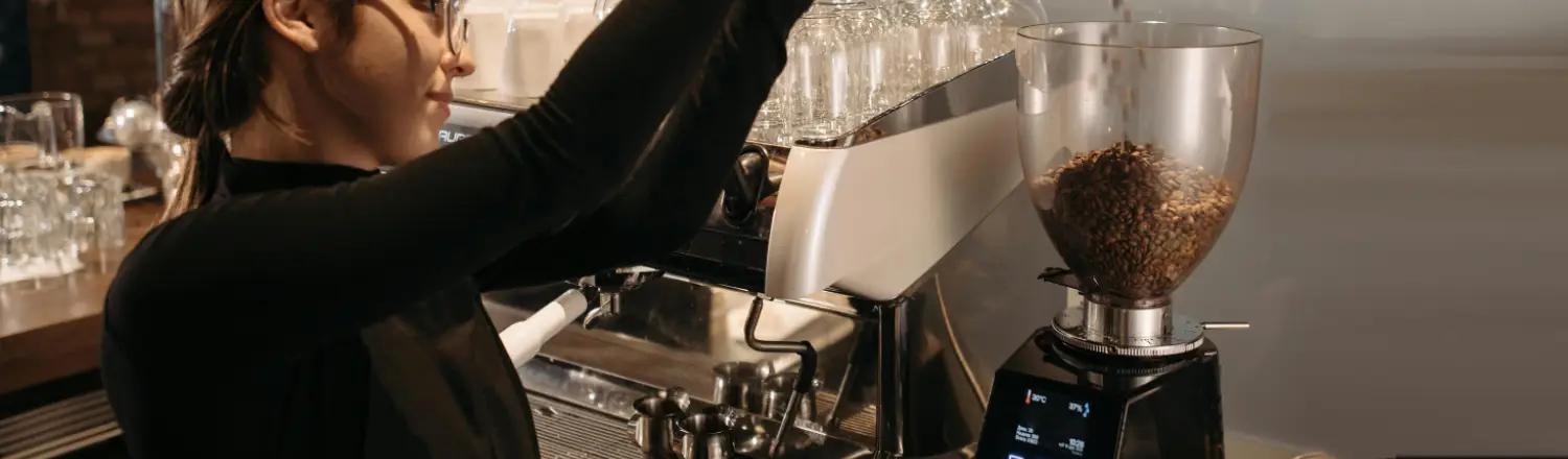 ☕ Conical vs Flat Burr Grinders: What’s the Difference? 2 Woman pouring coffee beans into a grinder in a modern kitchen setting.