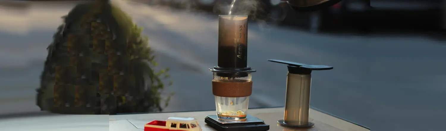 AeroPress XL Review: More Coffee, Same Great Brew ☕ 2 Person pouring water into an AeroPress sitting on a table outdoors