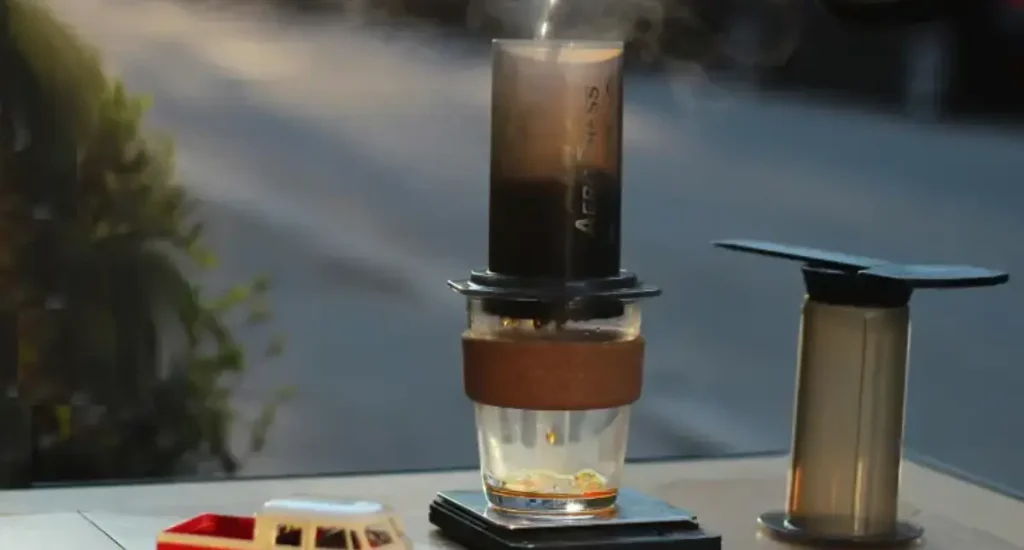AeroPress XL Review: More Coffee, Same Great Brew ☕ 67 Person pouring water into an AeroPress XL sitting on a table outdoors
