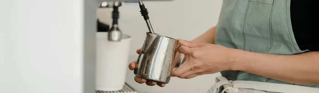 🥛 Best Milk Pitchers for Pouring Latte Art 188 Barista holding a milk pitcher under a steam wand to create microfoam for latte art