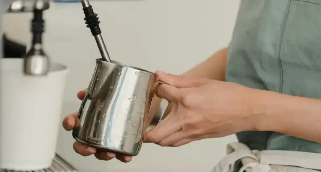 Best Milk Pitchers for Pouring Latte Art 🥛 159 Barista showing how to steam milk using a milk pitcher under a steam wand to create microfoam.
