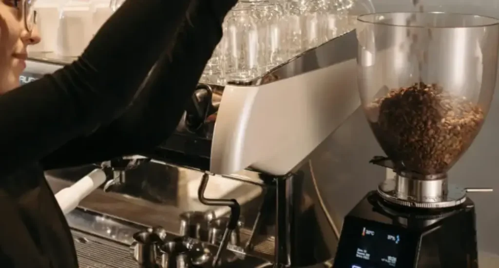 Conical vs Flat Burr Grinders: What’s the Difference? ☕ 157 Woman pouring coffee beans into a grinder in a modern kitchen setting.