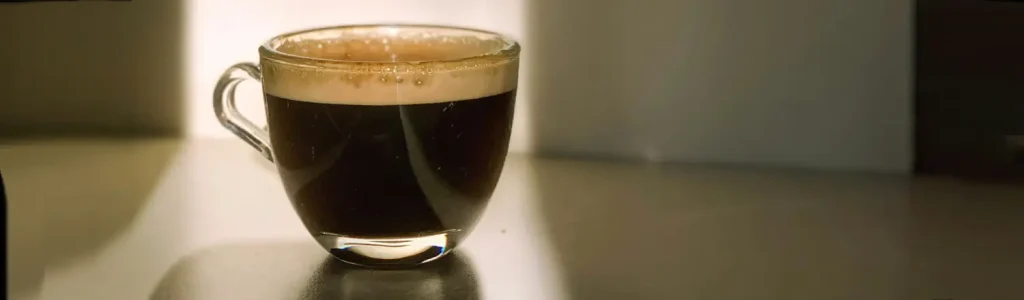 🇮🇹 What Is a Lungo? (Italian-Style Long Espresso Explained) 24 A freshly brewed lungo in a small glass cup sitting on a wooden table