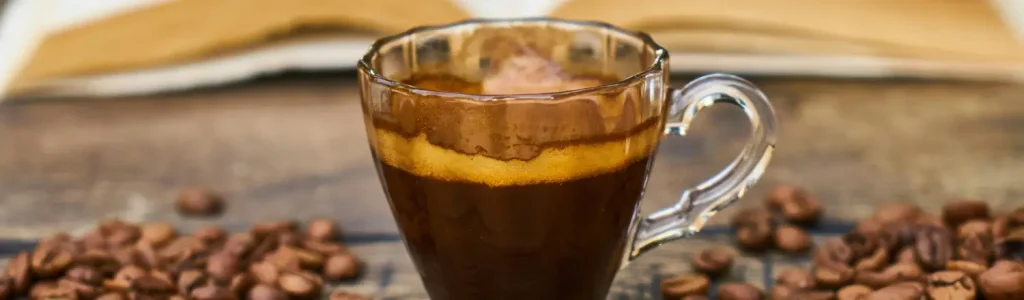 ☕ What Is a Red Eye Coffee? 22 A hot Red Eye Coffee in a ceramic mug on a wooden table surrounded by scattered coffee beans.