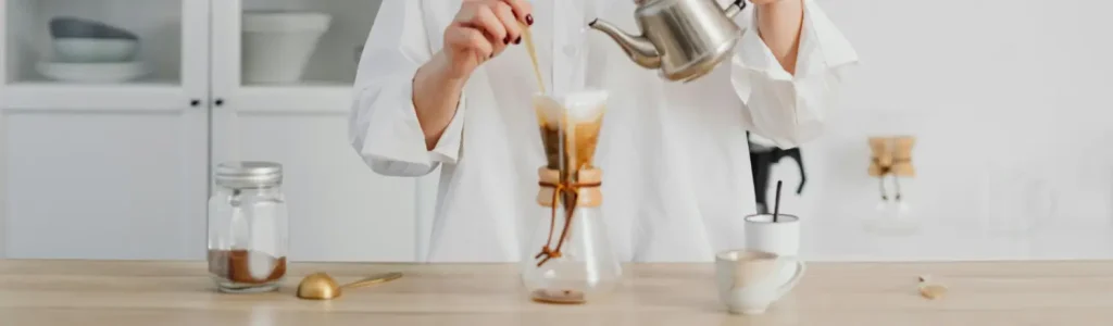 ☕Best Coffee Grinders for Pour-Over (Consistent Medium Grind) 116 Woman brewing pour over coffee with two cups and a container of coffee on the table