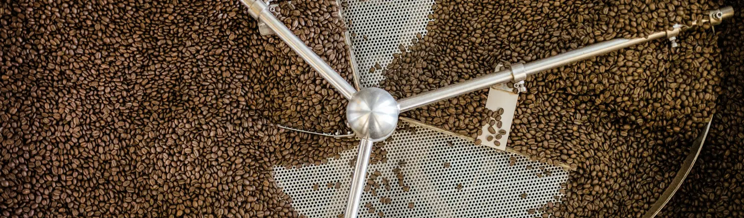 ☕ Coffee Roasts Explained: Light, Medium & Dark 2 Freshly roasted coffee beans pouring from a roaster into a hopper.
