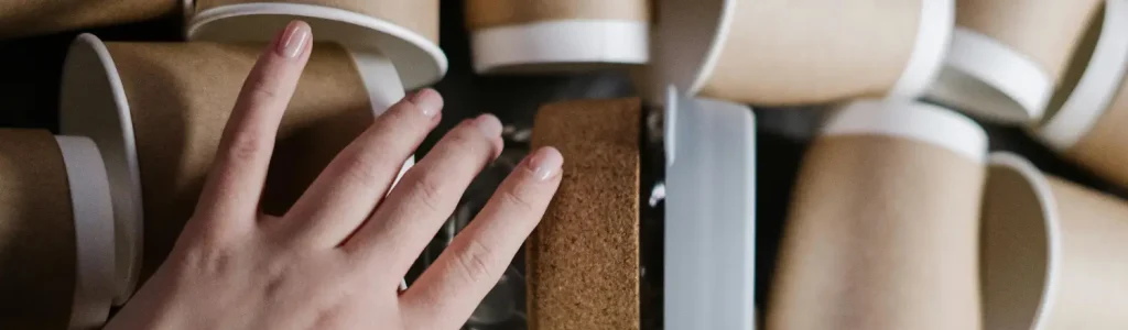 🌱 Eco-Friendly Home Barista Tips: Brew Better, Waste Less 97 Hand reaching for an eco-friendly reusable coffee cup among a stack of cups