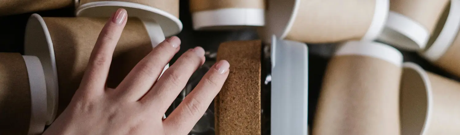 🌱 Eco-Friendly Home Barista Tips: Brew Better, Waste Less 2 Hand reaching for an eco-friendly reusable coffee cup among a stack of cups
