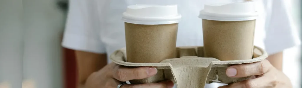 Eco-Friendly Coffee Gear & Sustainable Swaps ☕🌱 95 A person carrying two takeaway coffees in eco-friendly cups and a recyclable cardboard holder, symbolizing sustainable coffee habits.