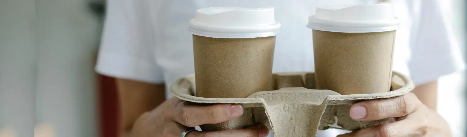 Eco-Friendly Coffee Gear & Sustainable Swaps βπ± 2 A person carrying two takeaway coffees in eco-friendly cups and a recyclable cardboard holder, symbolizing sustainable coffee habits.