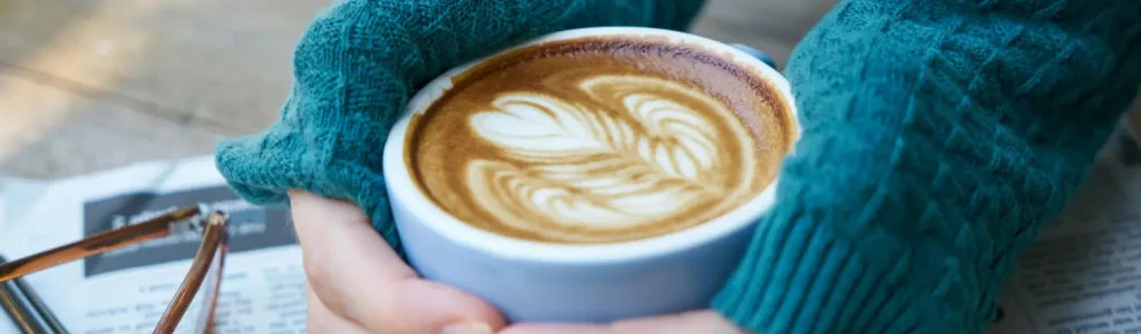 Why Your Homemade Lattes Don’t Taste Like the Café ☕ 46 Woman holding a warm latte in her hands, enjoying creamy homemade coffee at home.
