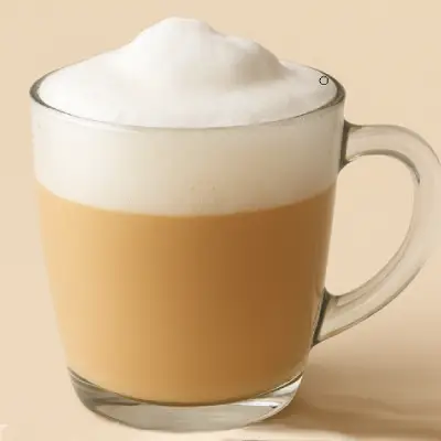 How to Make Perfect Latte Foam at Home A clear glass mug filled with a latte topped with thick, creamy foam, set against a warm beige background.