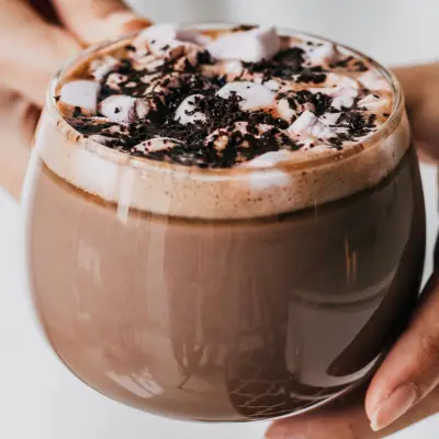 Woman Holding Creamy Hot Chocolate with a Barista Twist A woman holding a mug of creamy hot chocolate topped with frothy milk and cocoa, styled for a cozy barista-inspired drink.