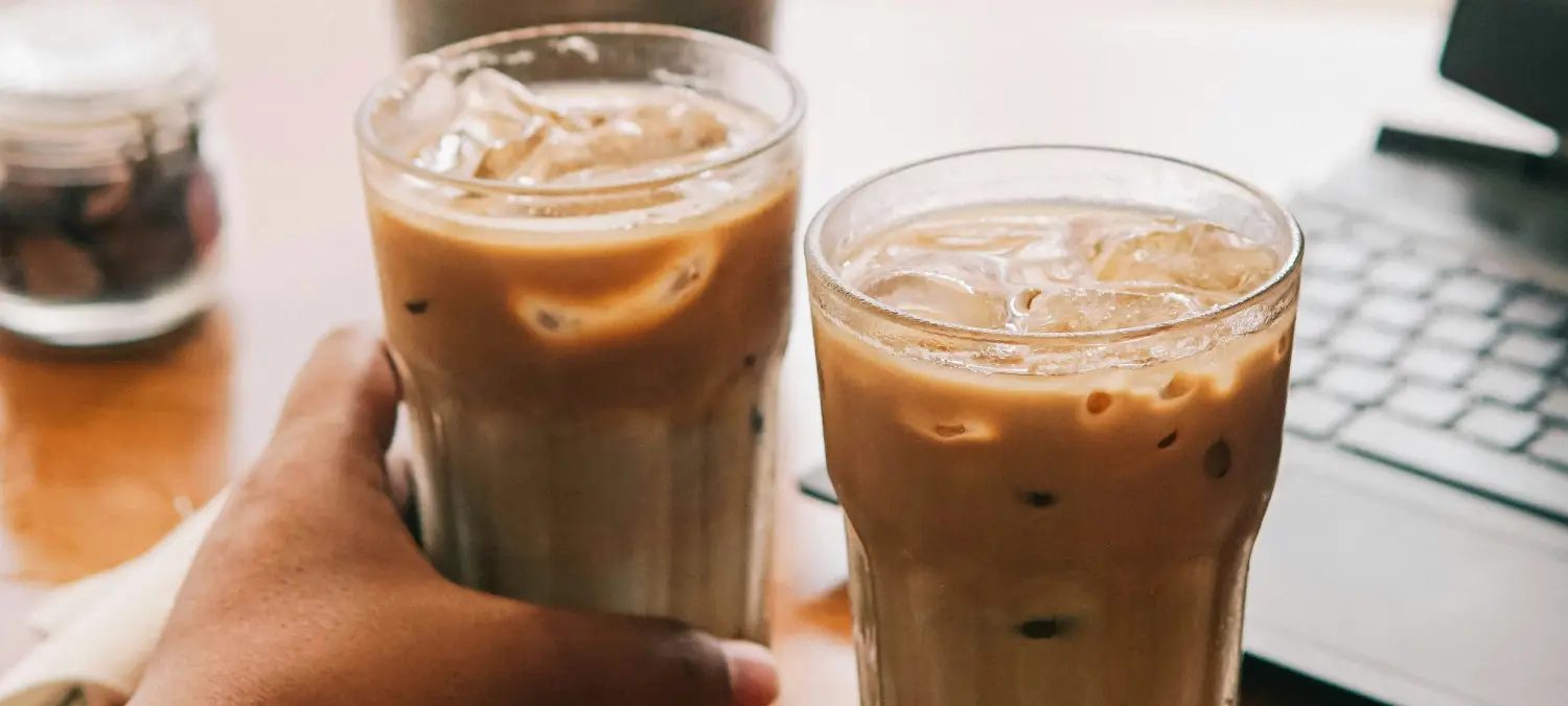 Iced Latte vs Cold Brew: What’s the Difference? ❄️ 2 Two iced lattes on a desk with a laptop, representing iced latte vs cold brew coffee drinks