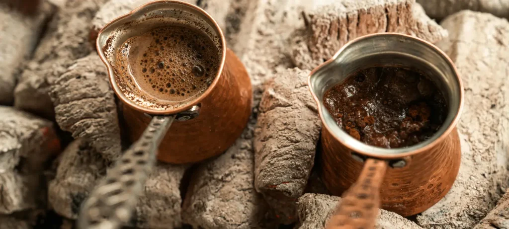 Greek Coffee 101: Brew, Taste & Cultural Traditions 🇬🇷 67 Two traditional Greek coffee brikis brewing coffee over hot coals