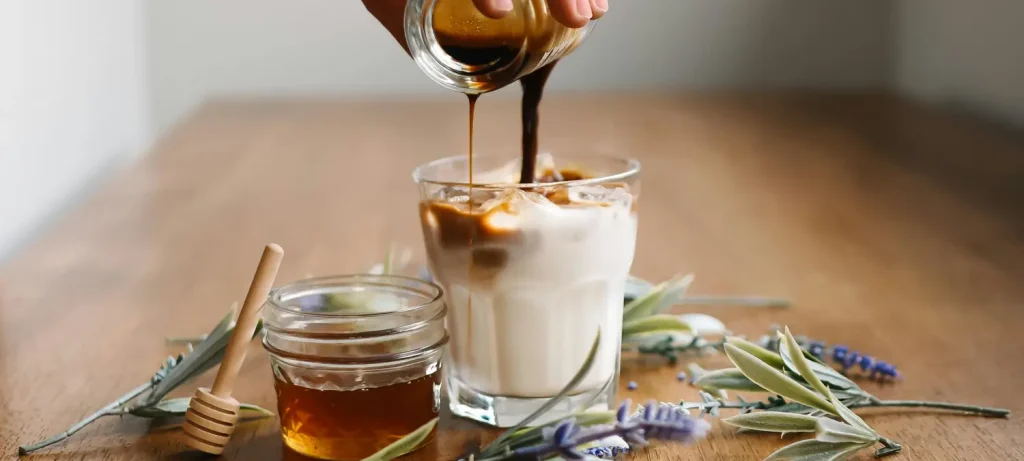 ☕ How to Sweeten Coffee Without Ruining the Flavor 58 Cup of coffee with a glass of honey beside it, showing how to sweeten coffee without ruining the flavor