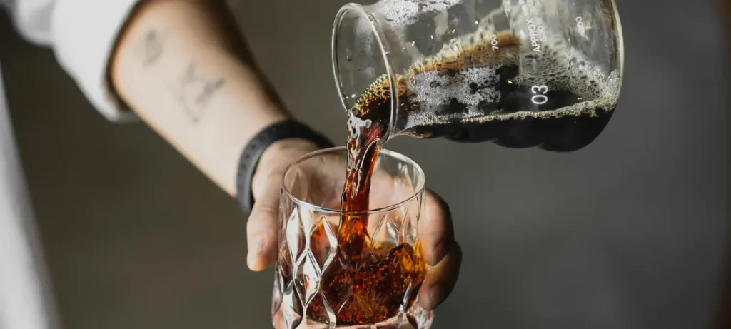 Best Coffee Makers for Cold Brew at Home 🏡 69 Man pouring cold brew coffee from glass carafe into a glass at home kitchen