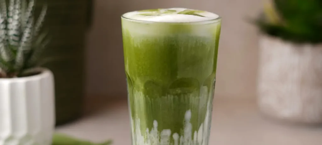 🍵 Matcha Latte vs Green Tea: What’s the Difference? (Taste, Caffeine + Health Explained) 55 Close-up of a creamy matcha latte in a glass showing vibrant green tea foam and smooth milk texture