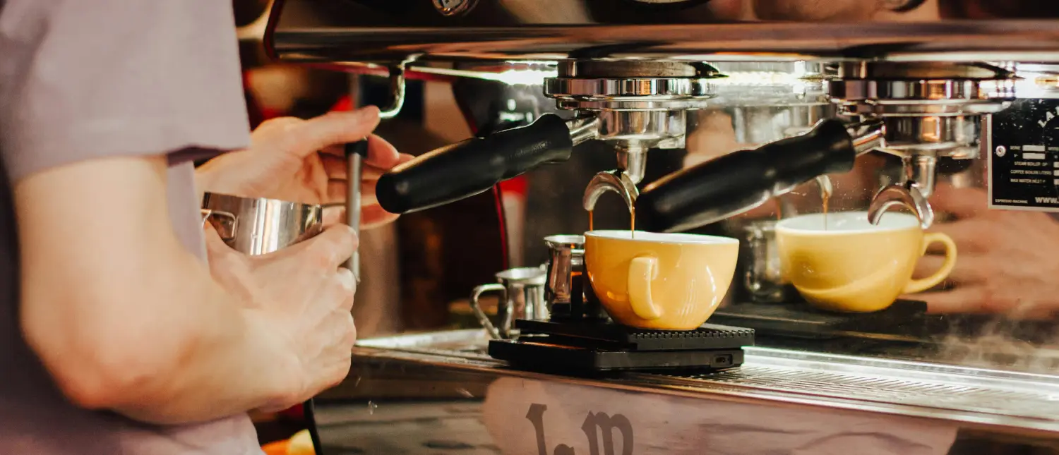 Best Brewing Methods for Low-Acid Coffee ☕✨ 2 Barista preparing a coffee drink using an espresso machine and steam wand for a smoother coffee experience