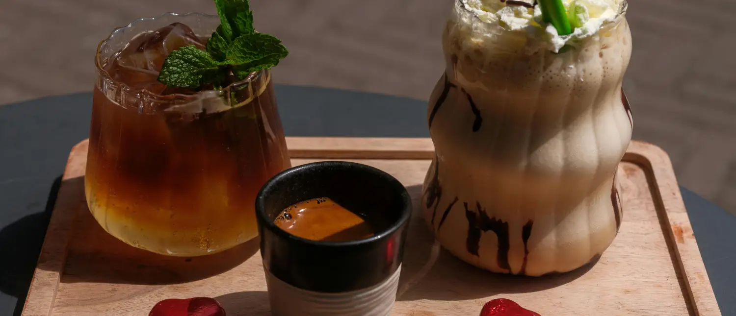 Hot vs Iced Coffee Drinks – What’s the Difference?☕🧊 2 Hot vs iced coffee side by side on a table with a plant showing the difference between hot and cold coffee drinks