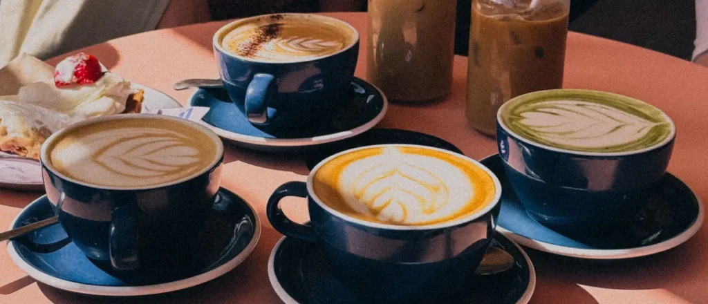 How to Make Café-Style Drinks at Home (Beginner Guide) 17 Variety of café-style coffee drinks arranged on a café table including lattes, cappuccinos, and iced coffee.