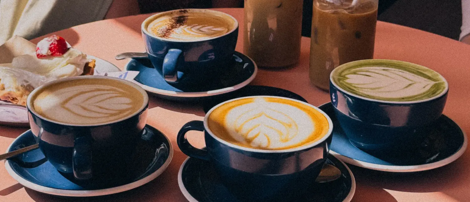 How to Make Café-Style Drinks at Home (Beginner Guide) 2 Variety of café-style coffee drinks arranged on a café table including lattes, cappuccinos, and iced coffee.