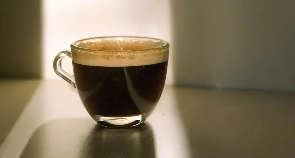 Lungo vs Espresso Explained: What’s the Difference? 4 A cup of freshly brewed espresso with rich golden crema beside roasted coffee beans, illustrating what espresso is for beginners.