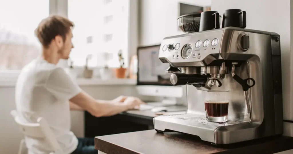How to Choose a Coffee Machine for Your Home 29 Young man researching how to choose a coffee machine for your home while sitting beside an espresso machine in a modern kitchen.